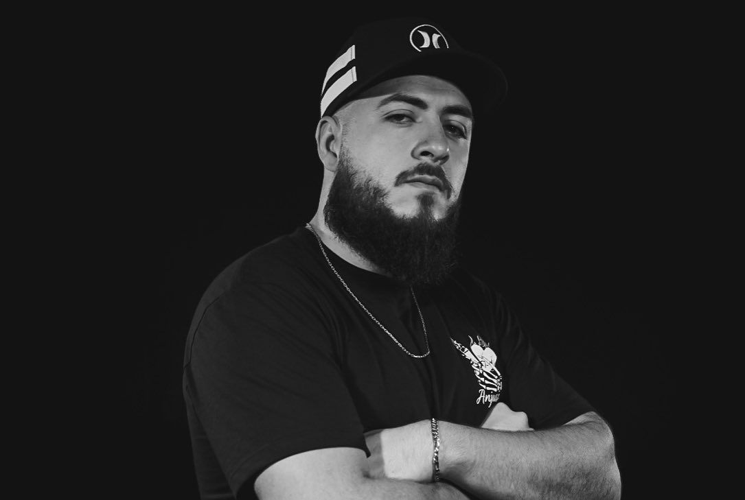Retrato em preto e branco do DJ Deivid Xister de braços cruzados